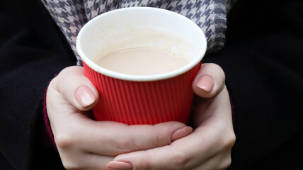 A young girl in a coat holds morning coffee with her while walking in the park. Hand holding paper...