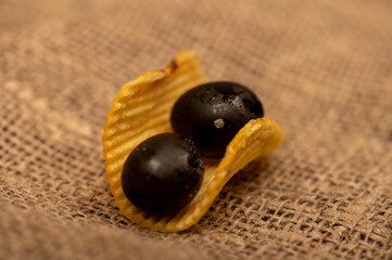 Crispy potato chips with olives on a coarse homespun cloth. Close up.