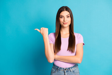 Photo portrait of shiny cute girl wear casual purple t-shirt pointing thumb empty space isolated blue color background