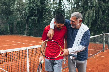 middle aged father with his son on tennis court