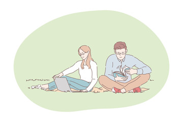 Picnic, relaxing, resting in park with book and laptop concept. Young happy couple sitting on blanket on grass in public park and relaxing with book and laptop during lunch break or weekend together
