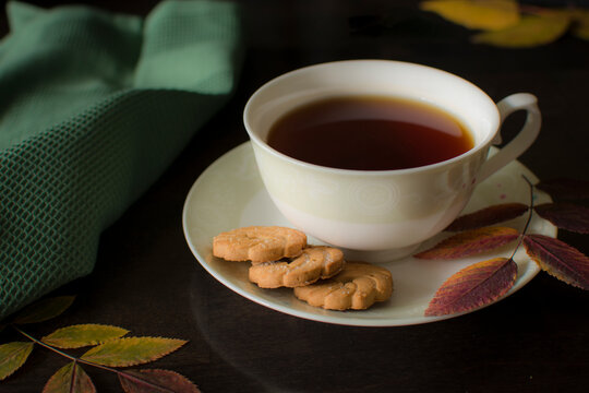 Black Tea With Cookies On A Dark Background With Yellow Oak Leaves. View From Above. The Photo Is Taken With Selective Focus And Has A Noise Effect.