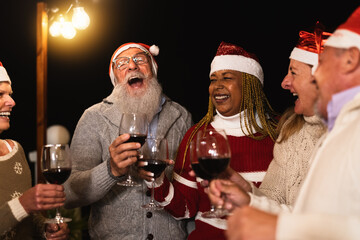 Happy multiracial senior friends celebrating Christmas holidays drinking red wine on house patio party