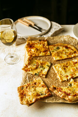 Homemade Belgian style four cheeses pizza, flammekeuche, on wooden board, glass of white wine