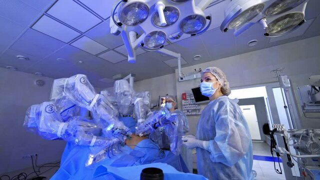 Surgery with robotic equipment in hospital. Minimally invasive surgery in modern operating room. Female doctor observes the work of robotic machine.
