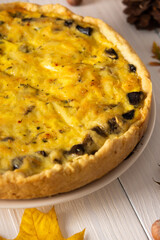 Quiche pie with mushrooms and cheese, autumn background with fallen maple and oak leaves, pine cones and hazelnuts