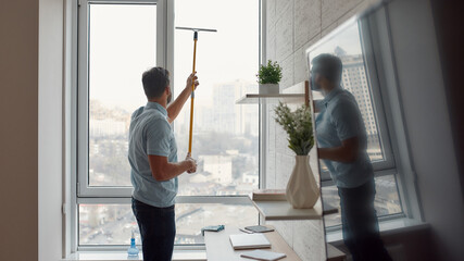 Fast and efficient. Male cleaner in uniform cleaning window with squeegee while working in the...