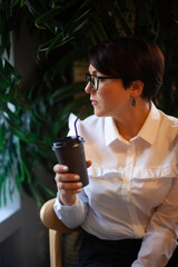 Happy young woman in business white blouse holding with hands a cup of healthy hot coffee latte