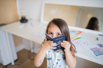 Little girl in front of a desk hides her face behind an American passport
