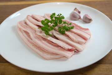 raw bacon with parsley on white plate