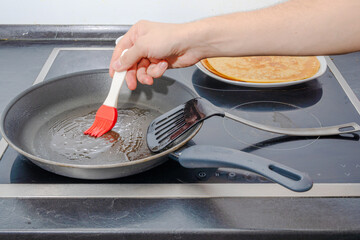 male human hand with red silicon brush put oil into hot pan to cook some Pancakes for breakfast