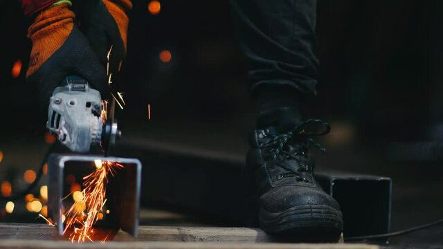 hands of a builder worker are holding a grinder and sawing metal at the factory.
