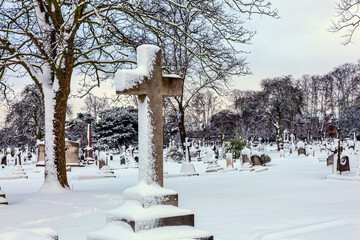 Cemetery winter cityscape with snow covered graveyard tombstone cross after a blizzard snowfall,...