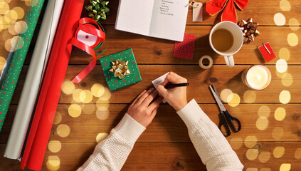 holidays, new year and christmas concept - hands packing gift box, attaching tag and writing...