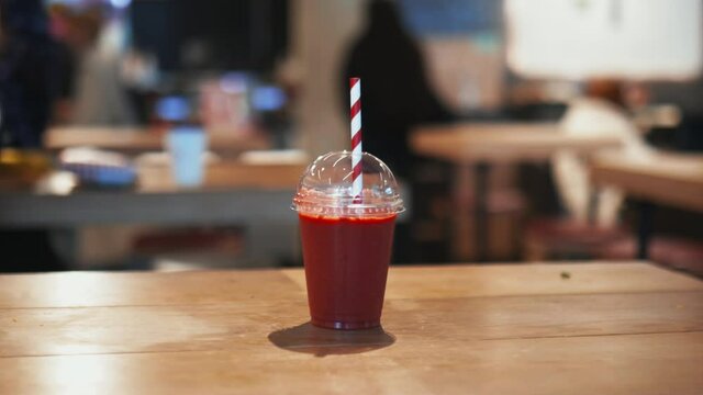Red smoothie with a red and white striped straw on a wooden restaurant table