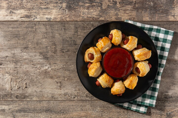 Pigs in blankets. Mini sausages wrapped in puff pastry with ketchup sauce on wooden table