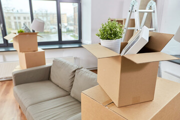 repair, moving and real estate concept - sofa and corrugated boxes with stuff at new home