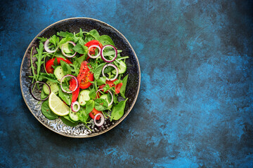 Diet salad of fresh vegetables and greens on a blue rustic background. Top view, flat lay, copy space.