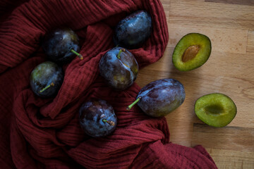 Fresh plums on red textured background. Top view photo of kitchen table. Autumn mood picture. Fresh plums on red textured background. Top view photo of kitchen table. Autumn mood picture. 