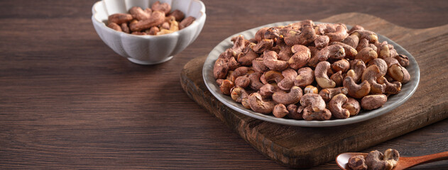 Cashew nuts with peel in a plate on wooden tray.