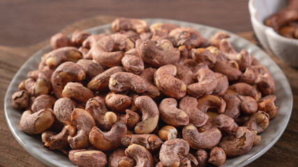 Cashew nuts with peel in a plate on wooden tray.