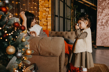 Little girl taking pictures of her mother at home, next to a christmas tree.