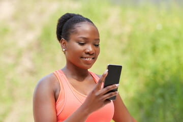 fitness, sport and technology concept - happy smiling young african american woman with smartphone exercising outdoors