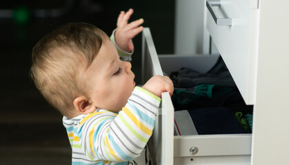 Little caucasian baby boy opening a white drawer with underwear when nobody is watching. Naughty...