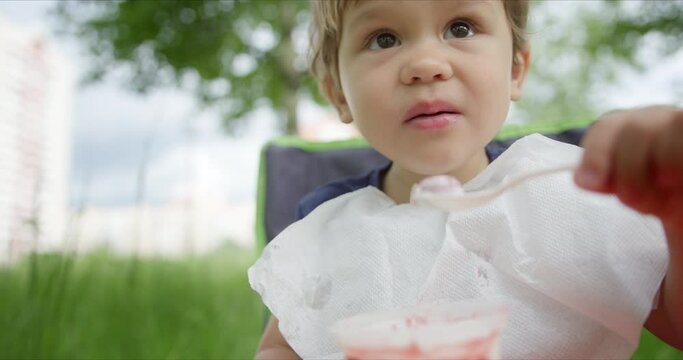 Litte girl eating ice cream with spoon in the park.