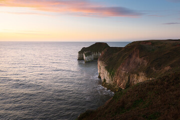 Sunrise over sea and eroded chalk cliffs under bright sky along coastline. Flamborough, UK.