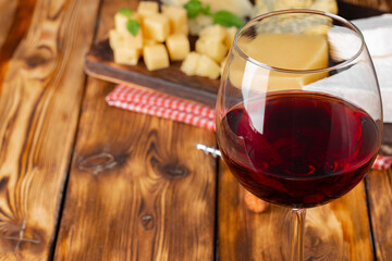 Red wine glass and cheese blocks on wooden table
