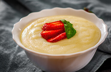 bowl of Semolina porridge with strawberries on wooden table