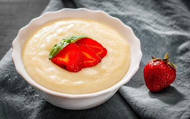 bowl of Semolina porridge with strawberries on wooden table
