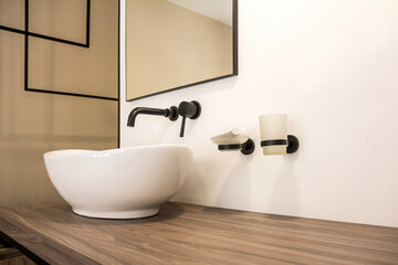 Contemporary bathroom sink. White washbasin in the form of a bowl on a wooden table in a modern hotel room.