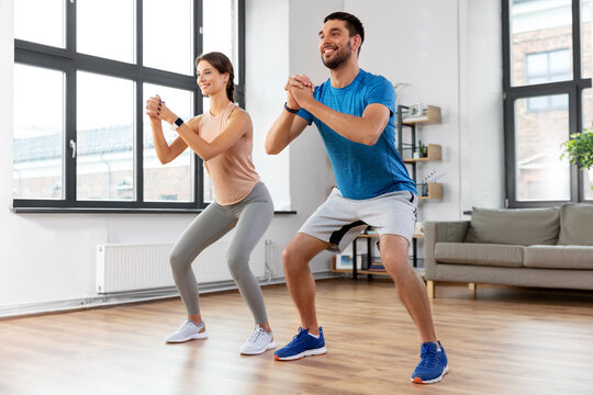 sport, fitness, lifestyle and people concept - smiling man and woman exercising and doing squats at home