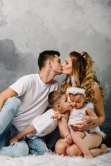 Happy family portrait in casual style clothes. Nice family wearing jeans isolated on grey wall. Smiling mother and father with daughter, son sitting on the floor. Fashion models plays with feathers.