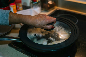Unrecognizable woman uncovering frying pan
