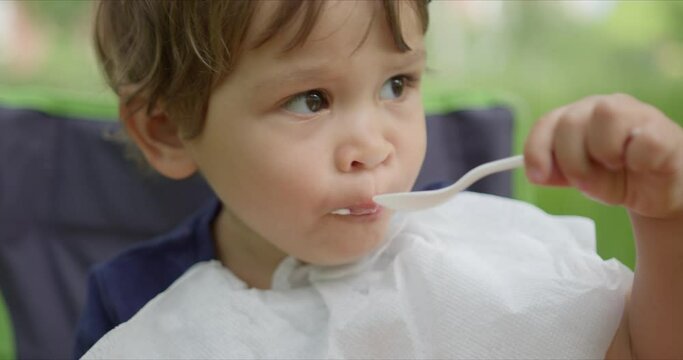 Litte girl eating ice cream with spoon in the park.