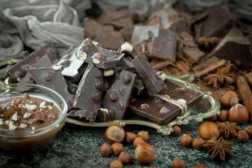 Dark chocolate in a composition with cocoa beans and nuts, on an old background.