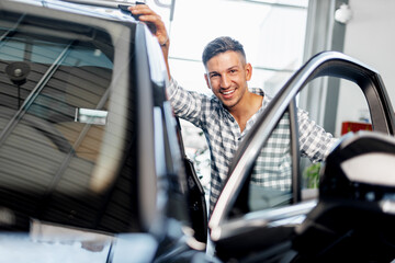 Cheerful young man customer buys a new car in a dealership