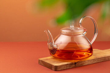 Glass teapot with black tea on background of blurred foliage