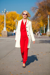 Young beautiful woman in a beige coat walks in the autumn park