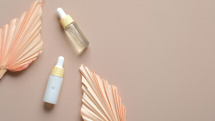 Dropper bottles with serum and essential oil and dry flower leaves on paste beige background. Natural organic lotions.