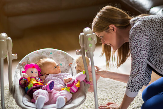 Woman Playing With Baby Surrounded By Toys Lying In Baby Swing