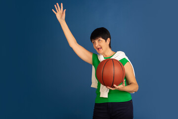 Playing basketball. Portrait of senior woman in stylish outfit isolated on blue studio background. Tech and joyful elderly lifestyle concept. Trendy colors, forever youth. Copyspace for ad.