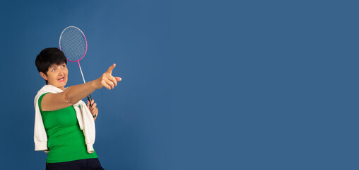 Playing badminton. Portrait of senior woman in stylish outfit isolated on blue studio background....