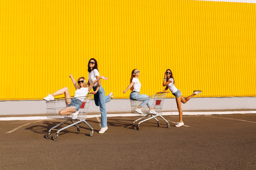 Image of young smiling women friends having fun with shopping cart in city near shopping mall