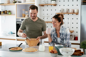 Husband and wife making pancakes at home. Loving couple having fun while cooking