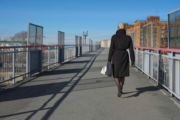 woman in black coat walks across the bridge in the city