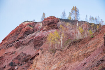Red mountains with autumn trees and blue cloudy sky. Colored waste heaps after extracting coal from...